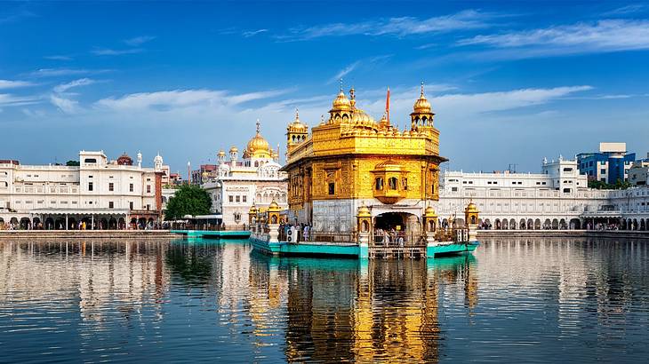 A golden temple floating in a body of water with buildings at the back