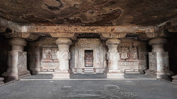Inside of an old Buddhist cave with small columns and carvings of Buddha Inside of an old Buddhist cave with small columns and carvings of Buddha