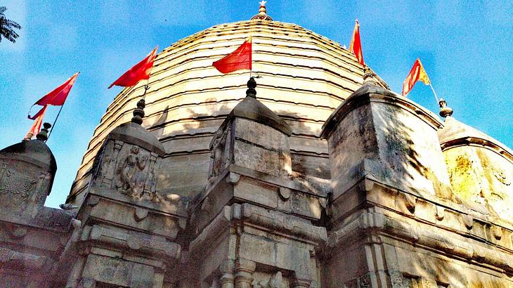 A temple's dome with red flags from below against a blue sky