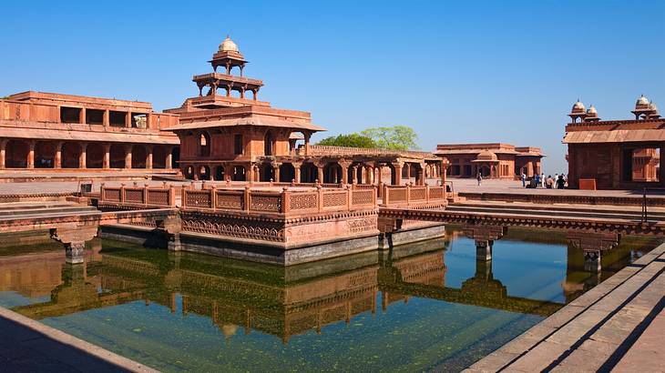 A small town in India full of red sandstone buildings with a pool of water in front