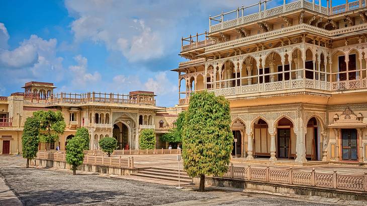 The exterior of a sandstone palace with a courtyard and green trees in front The exterior of a sandstone palace with a courtyard and green trees in front