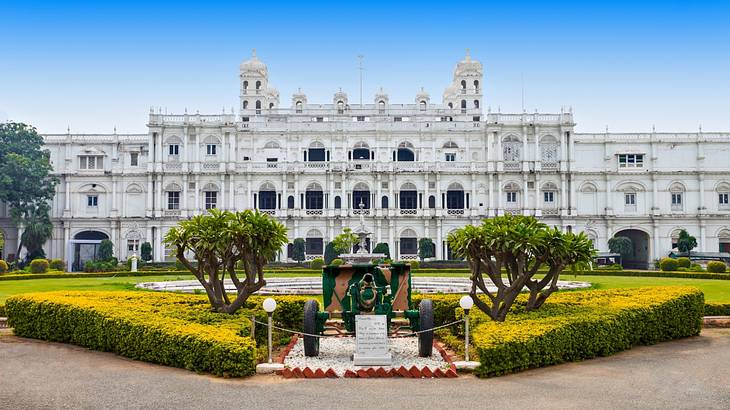 A large white palace-like building with a manicured green garden in front A large white palace-like building with a manicured green garden in front
