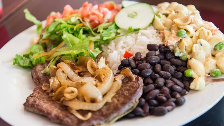 Pork with onions, black beans, white rice, and vegetables served on a white plate