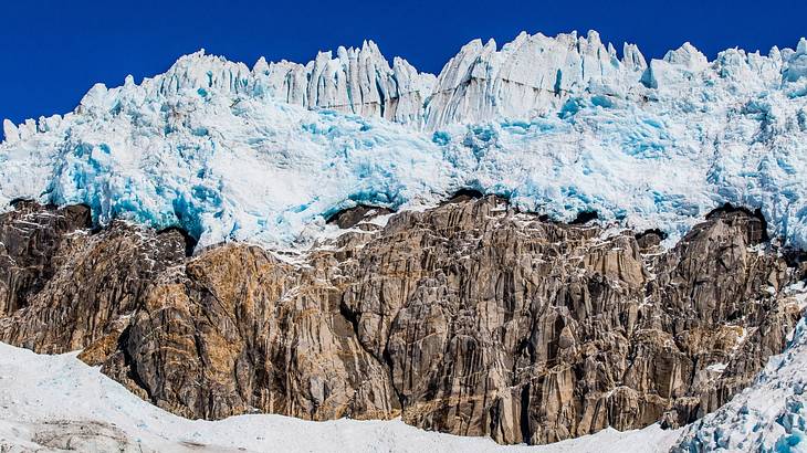 Gigantic ice towers above a rocky cliff against a clear blue sky