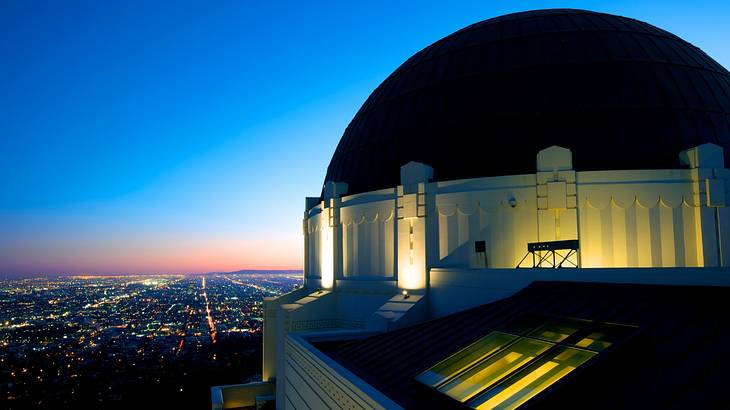 A dome-shaped white building with lights overlooking the city at dusk A dome-shaped white building with lights overlooking the city at dusk