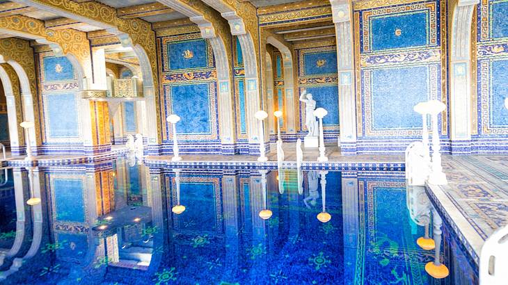 A luxurious Roman-style indoor pool with blue mosaic tiles and white statues