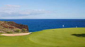 A green grassy golf course on a cliff with a view of the ocean