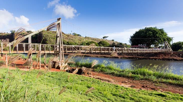 Wooden suspension bridge over a river with a blue sky and clouds in the background
