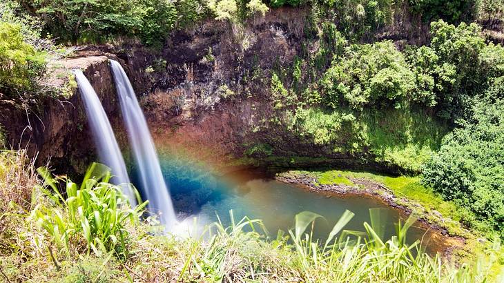 High-angle shot of a rainbow near the base of waterfalls in a tropical landscape