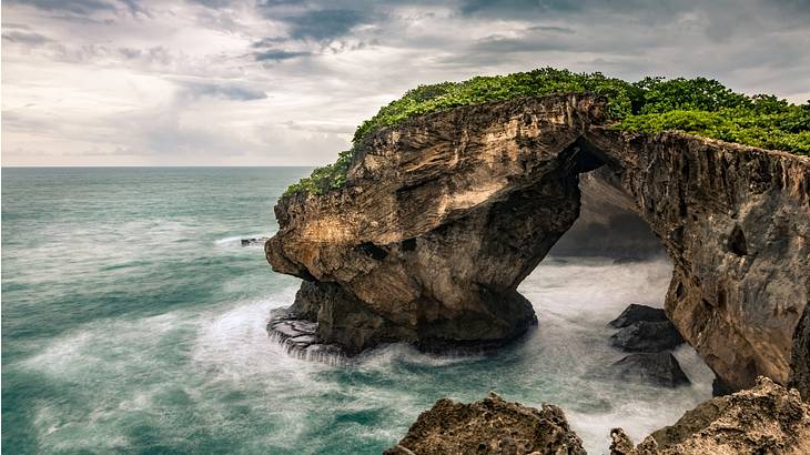 Stunning cave surrounded by dramatic cliffs facing the ocean on a gloomy day