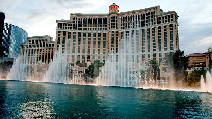 Fountains spraying out of a pond in front of a regal hotel and blue sky