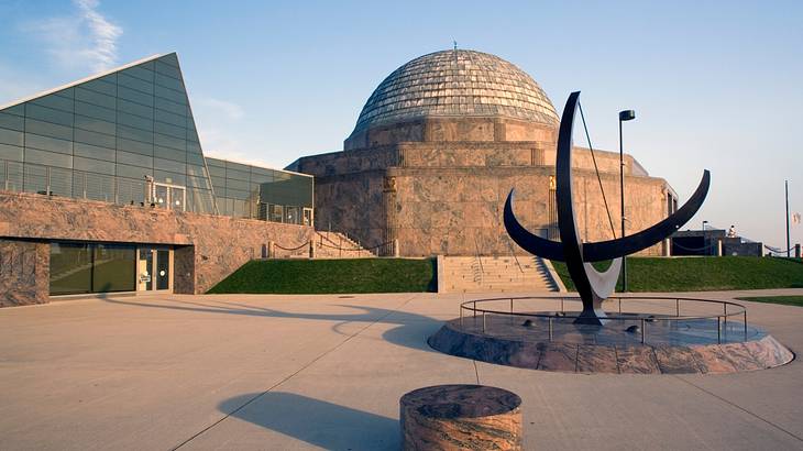 A planetarium with a dome roof next to a glass building with a sculpture in front