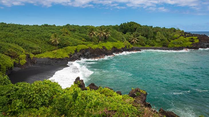 A black sand beach surrounded by blue ocean, greenery covered mountains, and blue sky A black sand beach surrounded by blue ocean, greenery covered mountains, and blue sky