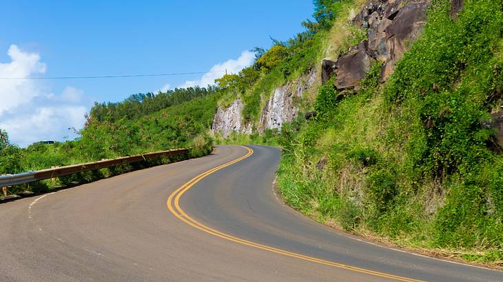A winding road surrounded by mountains covered with greenery and blue sky A winding road surrounded by mountains covered with greenery and blue sky