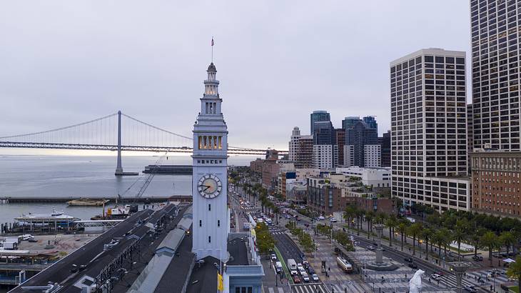 A tall white building with a clock near a pier and with buildings behind A tall white building with a clock near a pier and with buildings behind