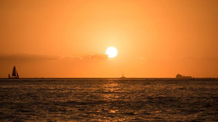 Silhouette of a few sailboats on the ocean with the sun setting in the background