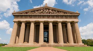 A Greek-style Parthenon with blue sky behind and path and grass in front.