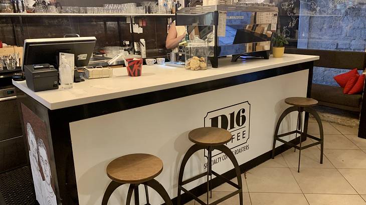 The inside of a coffee shop with a coffee machine on a counter and 3 stools in front