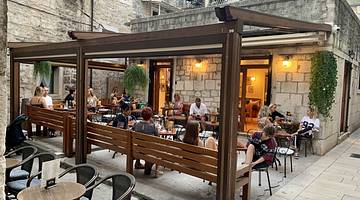 People sitting at tables and chairs under a wooden structure in a courtyard