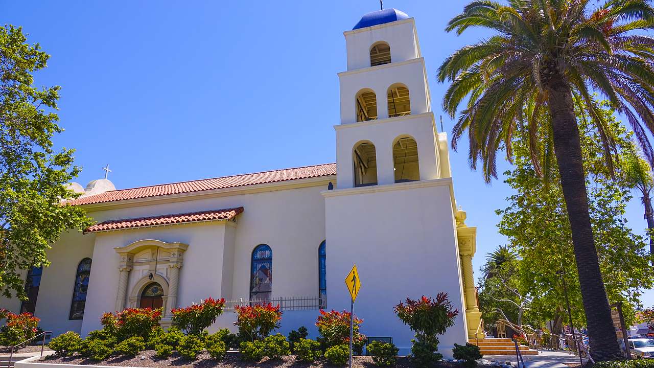 Spanish era old church with palm trees and plants around under a clear sky