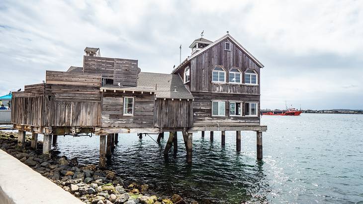 Old wooden house over water with rocks at the bottom, under an overcast sky