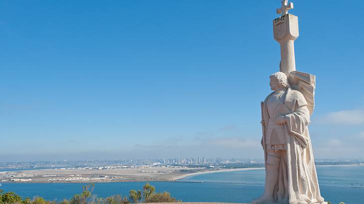 White statue with a cross on top overlooking the ocean under a clear blue sky