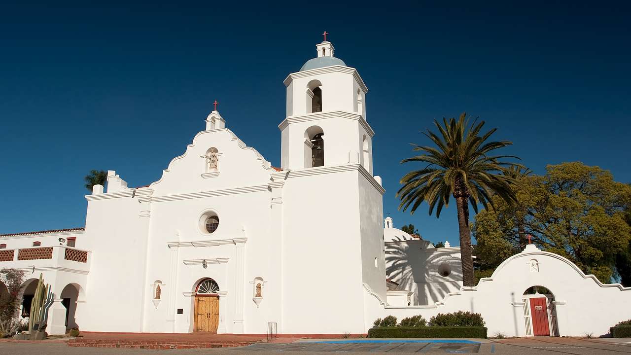 White church with Spanish-era architecture and trees nearby and a clear sky