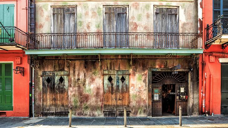 An old building with a faded wood exterior, iron balcony, and windows with shutters