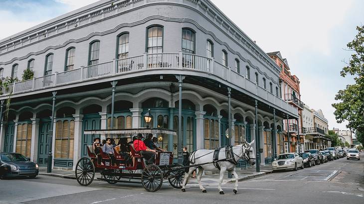 A horse and carriage on a road in front of an old fashioned New Orleans building