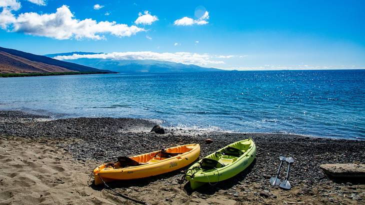 Two kayaks sitting on the sand surrounded by ocean and blue sky
