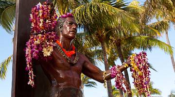 Bronze statue of a man with a surfboard and leis placed on it