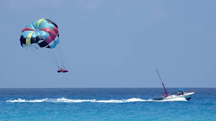 A boat with someone parasailing on the ocean under blue sky