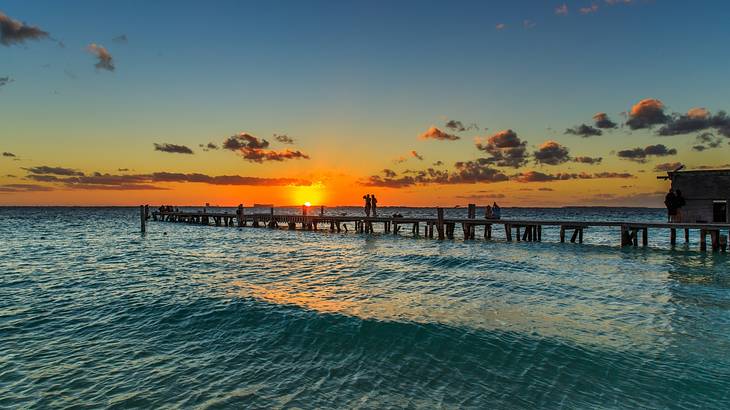 The ocean with a boardwalk bridge under a sky with the sun setting