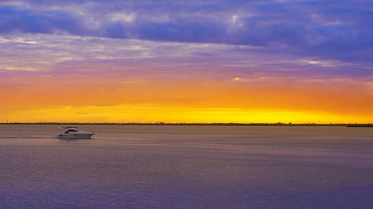 A purple and orange sunset over the ocean with a boat on the water