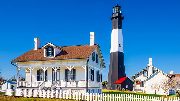 A small white house with a black and white lighthouse and other buildings next to it. A small white house with a black and white lighthouse and other buildings next to it.