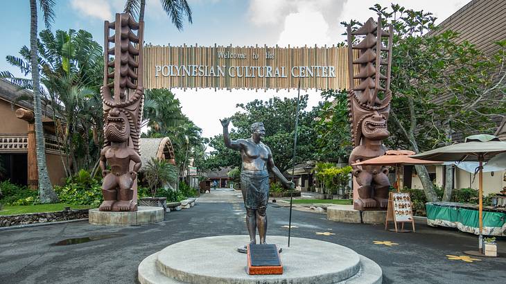 A sign for Polynesian Cultural Center with Hawaiian sculptures and statues