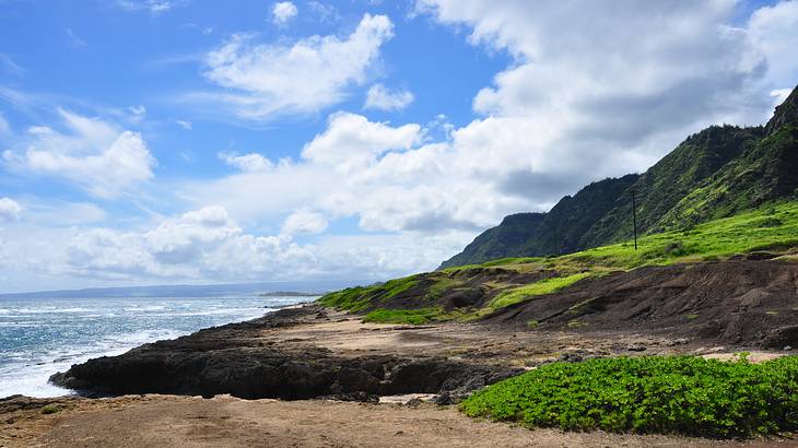 Mountains with greenery and the ocean to the side under a blue sky with clouds