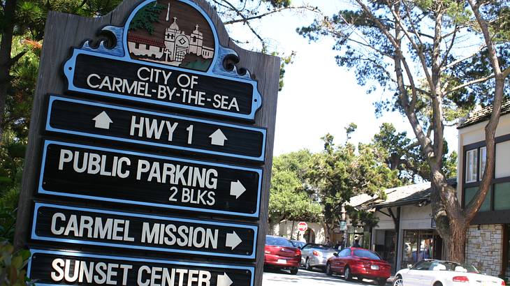 "City of Carmel-by-the-Sea" signage shaded by trees, on a street with parked cars