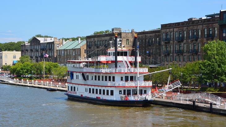 A white and red riverboat on the water with buildings behind it