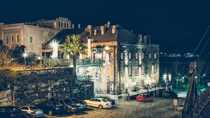 A stone building with cars parked in front of it and water to the side at night A stone building with cars parked in front of it and water to the side at night