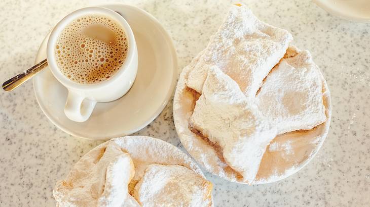 A table with small coffee cup and beignets covered in powdered sugar A table with small coffee cup and beignets covered in powdered sugar