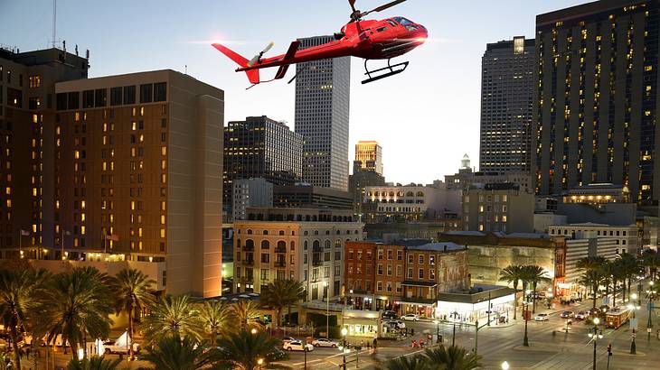 A red helicopter flying over a city with tall buildings and streets below