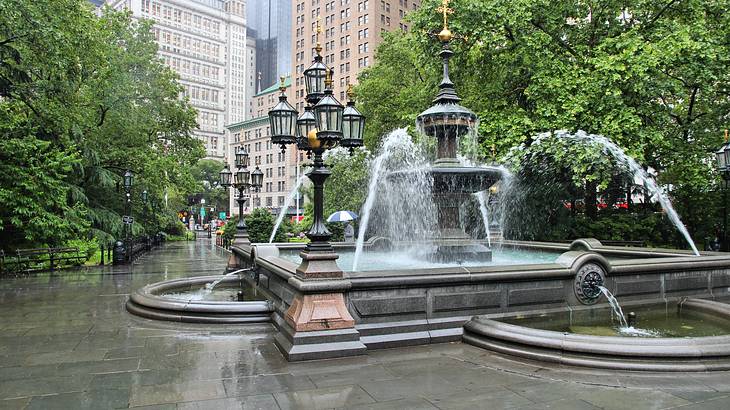A water fountain with trees surrounding it and buildings in the background
