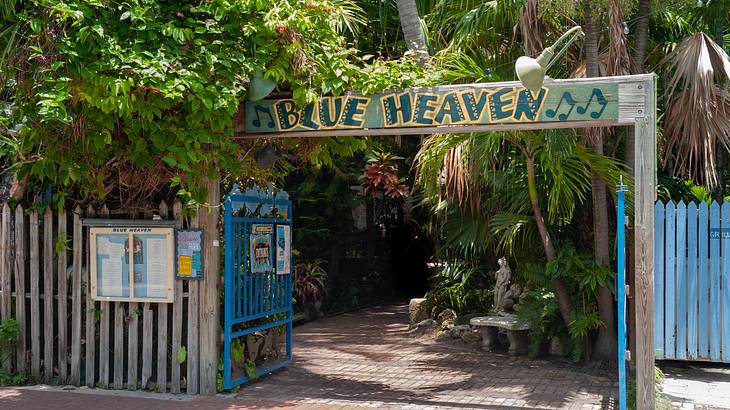 An outdoor entrance way with a Blue Heaven sign, wooden gate, and tropical greenery