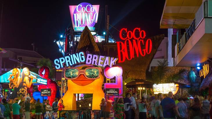 People standing outside Coco Bongo nightclub that's covered with bright signs