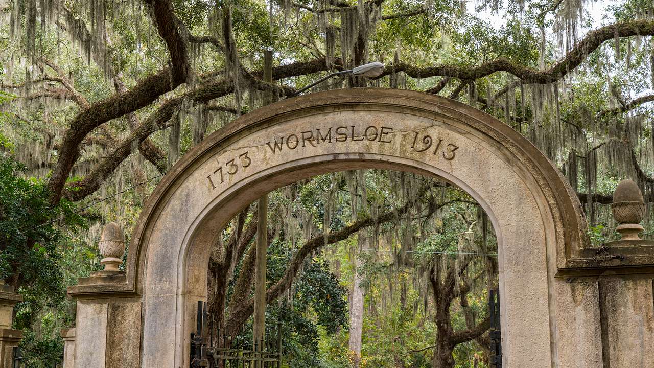 An old stone arch gate that says Wormsloe with trees surrounding it