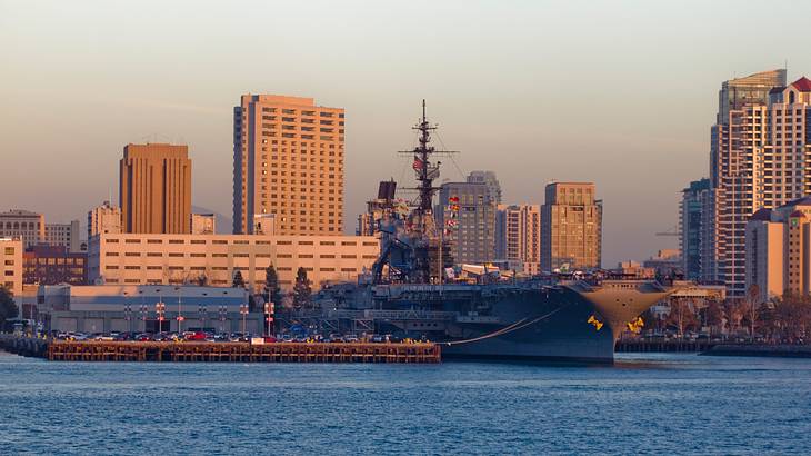A military ship docked in a pier with skyscrapers in the background