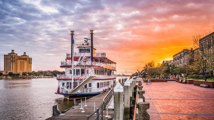 A river with riverboat on it and street and buildings to the side under a sunset