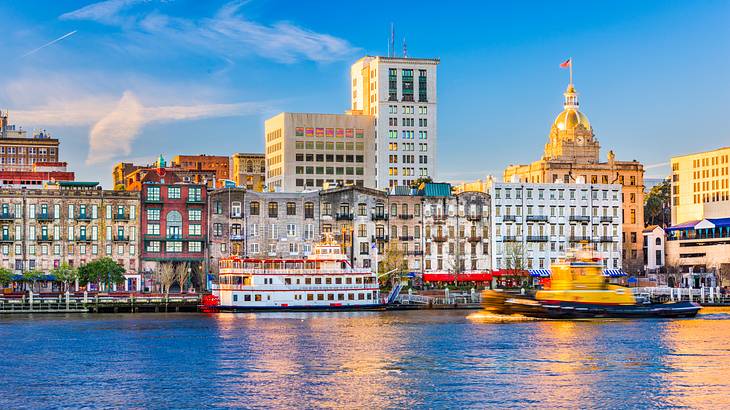 A line of buildings with a river and river boats in front of them under a blue sky