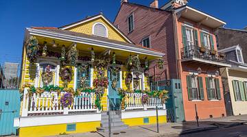 A small yellow house with yellow, purple, and green Mardi Gras decorations